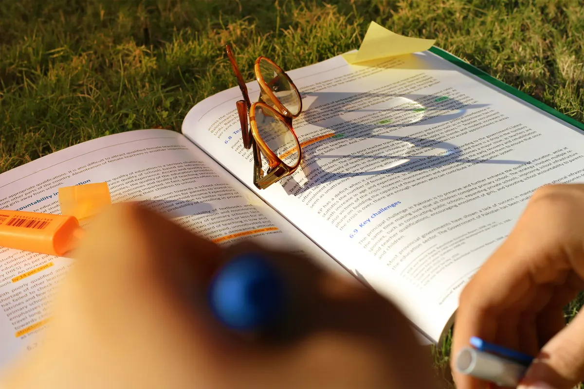 Estudiante subrayando un texto de estudio al aire libre